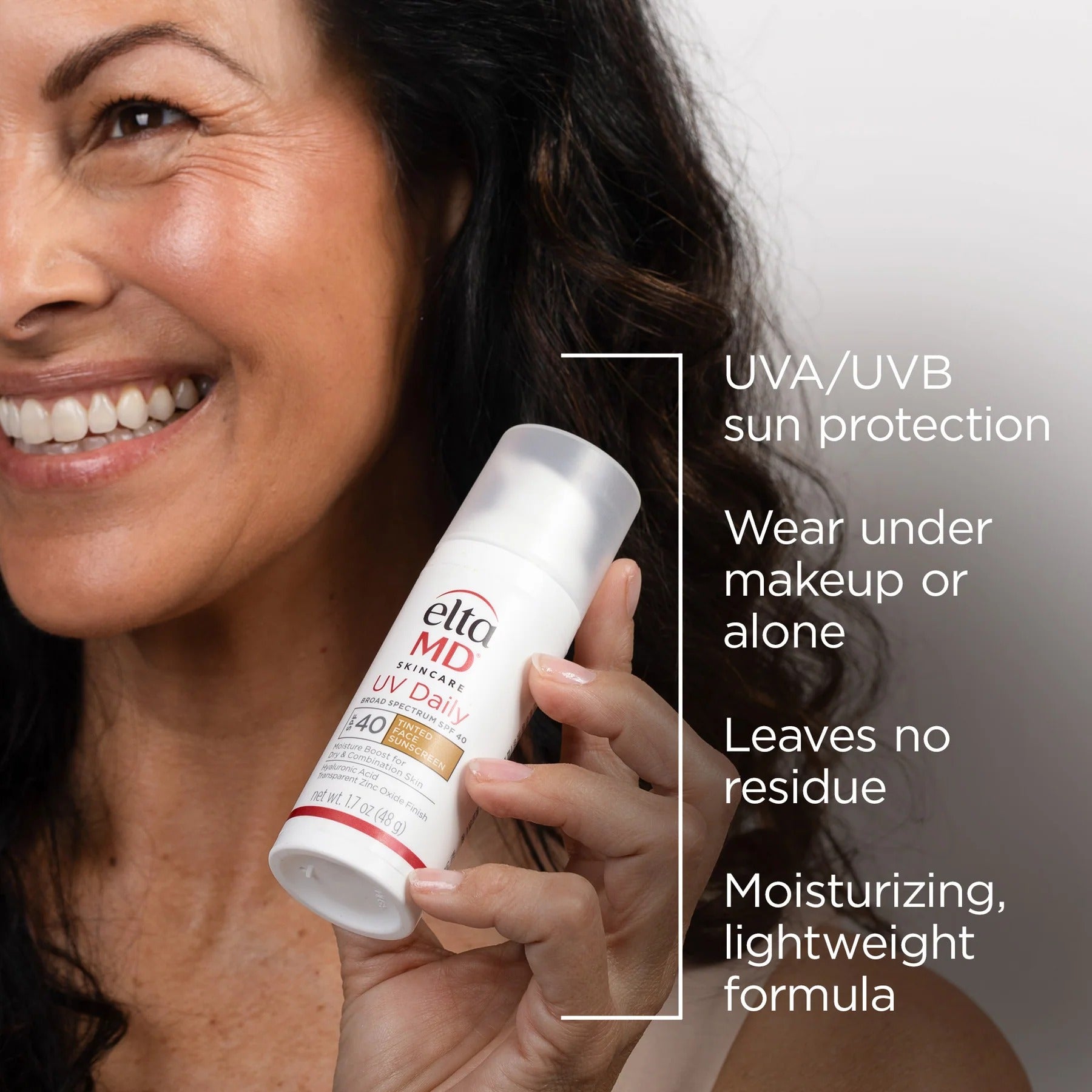 Woman holding a bottle of Elta MD UV Daily sunscreen with product features listed.
