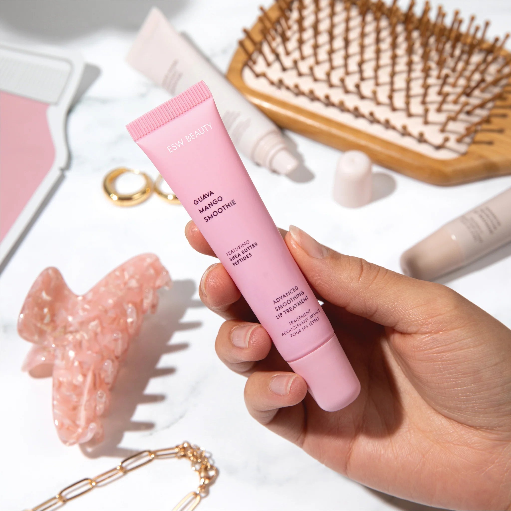 Hand holding a pink skincare tube with a blurred background of beauty products.