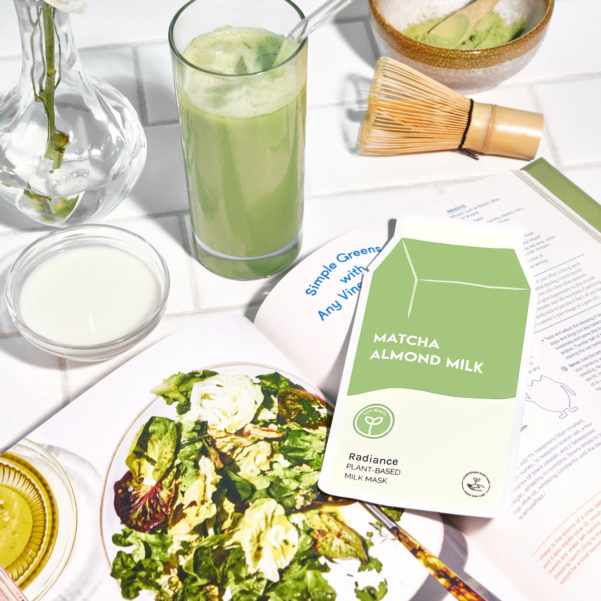 Matcha almond milk package with a glass of matcha, salad, and other items on a table.