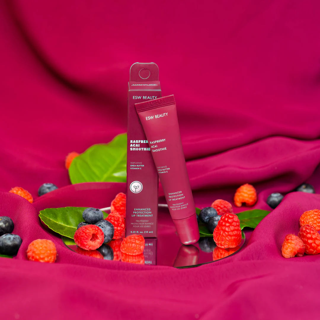 The Pharmacy Lab ESW Beauty Raspberry Acai Smoothie Enhanced Protection Lip Treatment displayed with packaging, raspberries, and blueberries on a vibrant pink backdrop