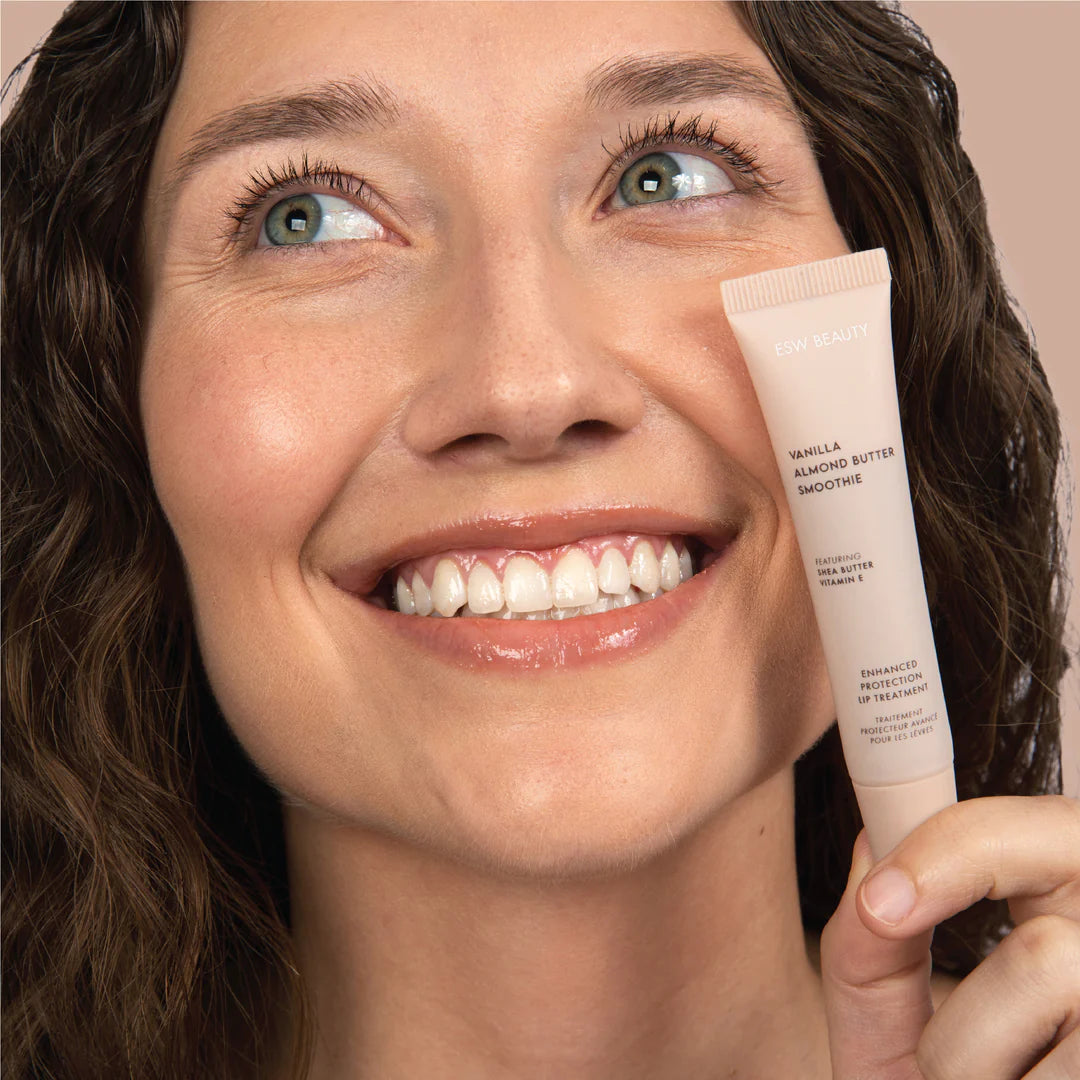 Woman holding a skincare product close to her face against a neutral background