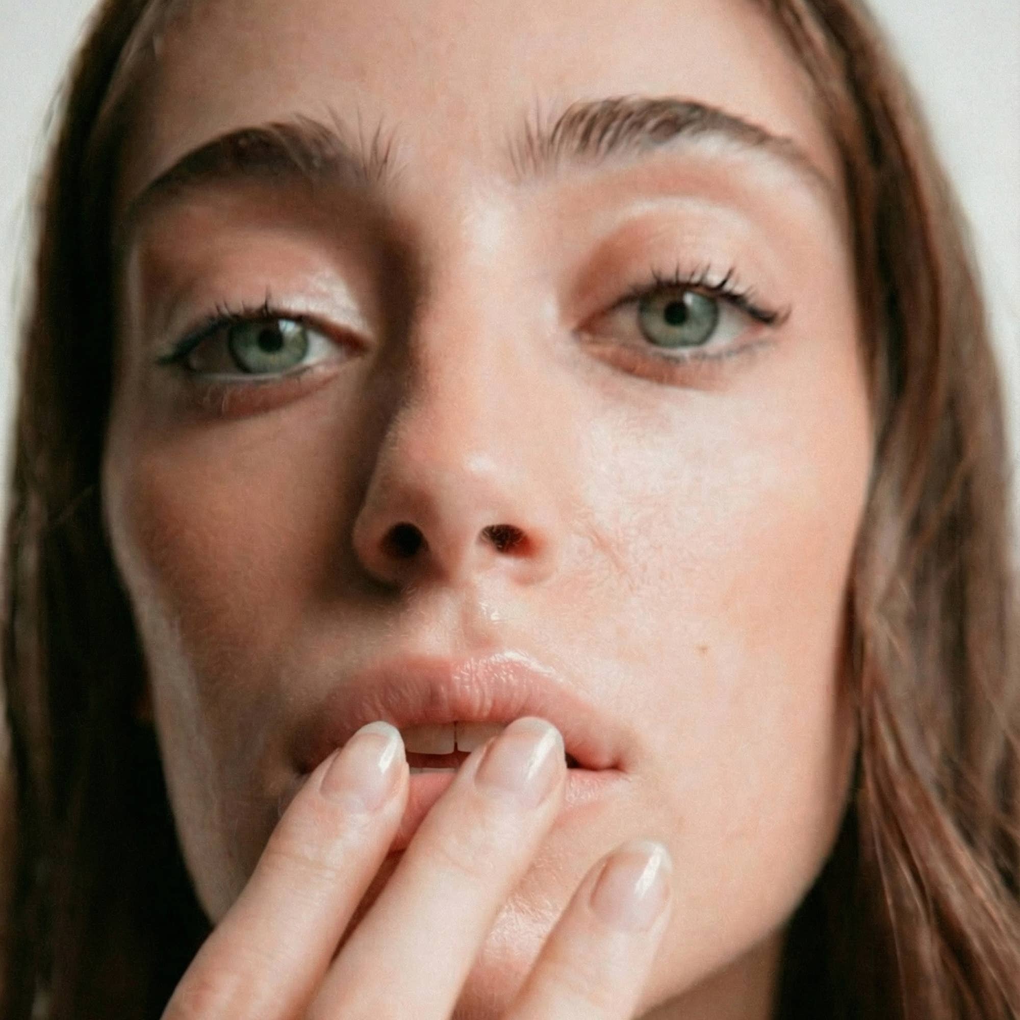 Close-up of a woman with her hand near her mouth against a neutral background