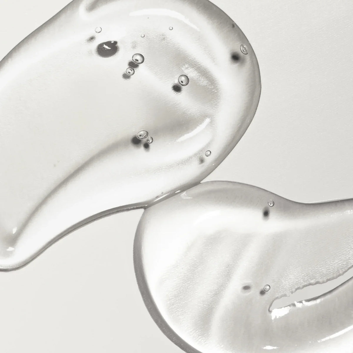 Close-up of two droplets of clear gel or serum on a light gray background
