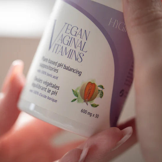 Hand holding a container labeled 'Vegan Vaginal Vitamins' with a blurred background.