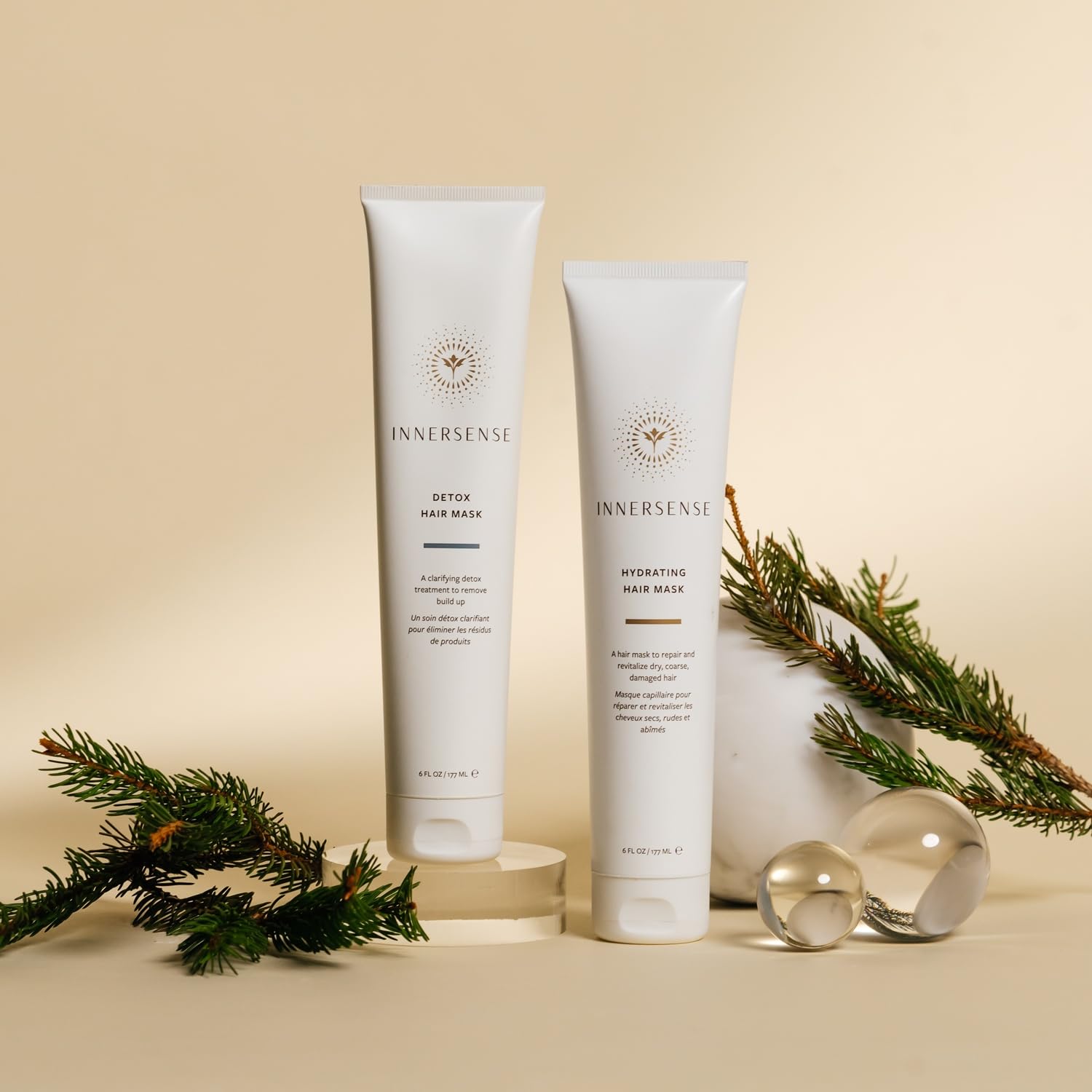 Two Innersense hair mask bottles with decorative greenery on a beige background