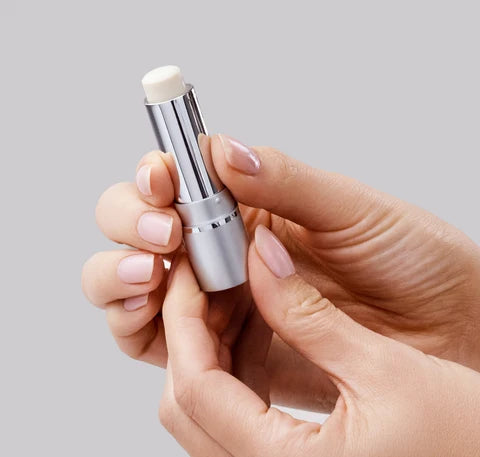 Hand holding a silver lip balm stick against a light gray background