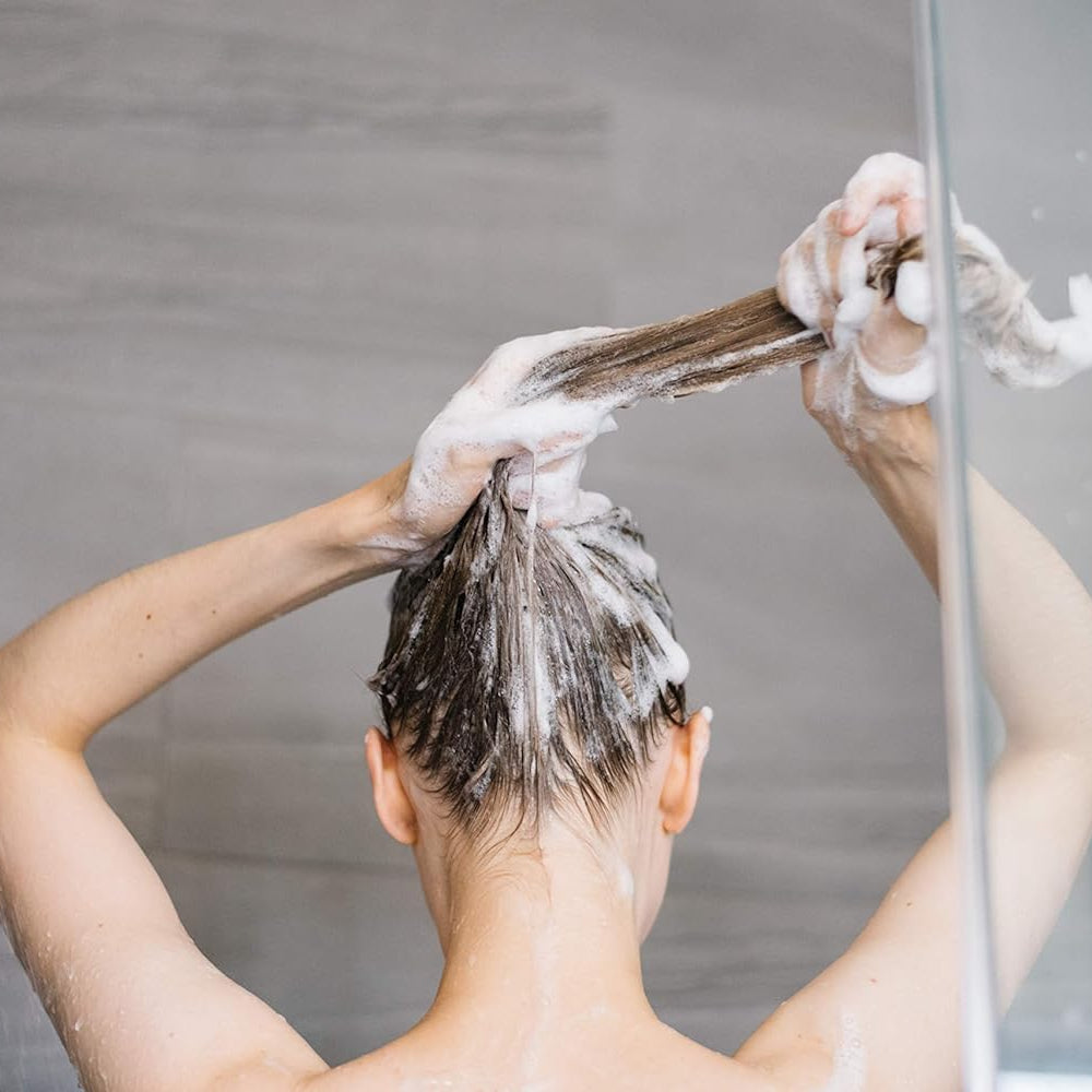 Person washing hair with shampoo in a shower