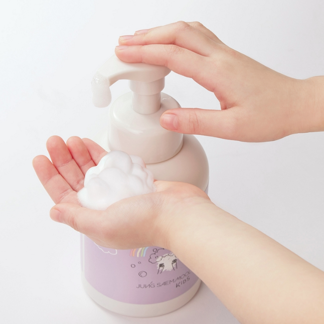 Hand using a white pump bottle to dispense soap onto a hand against a light background