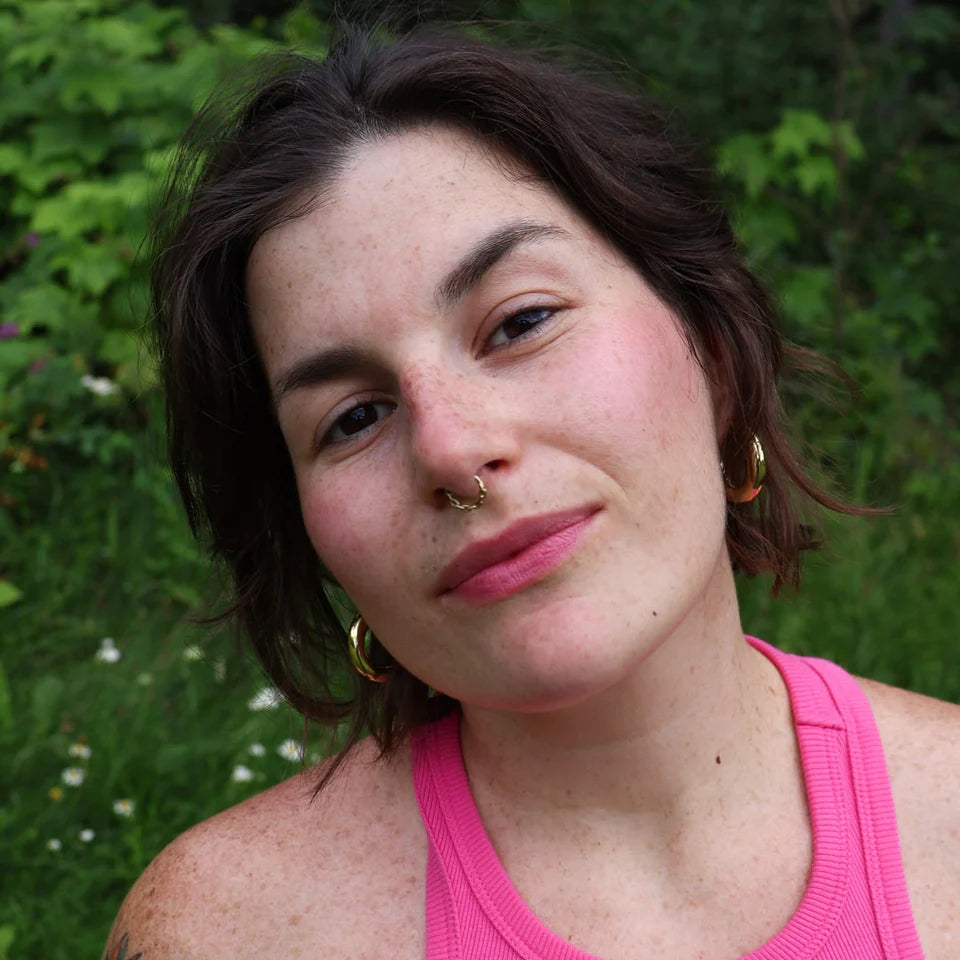 Woman with short brown hair and pink top standing in front of green foliage