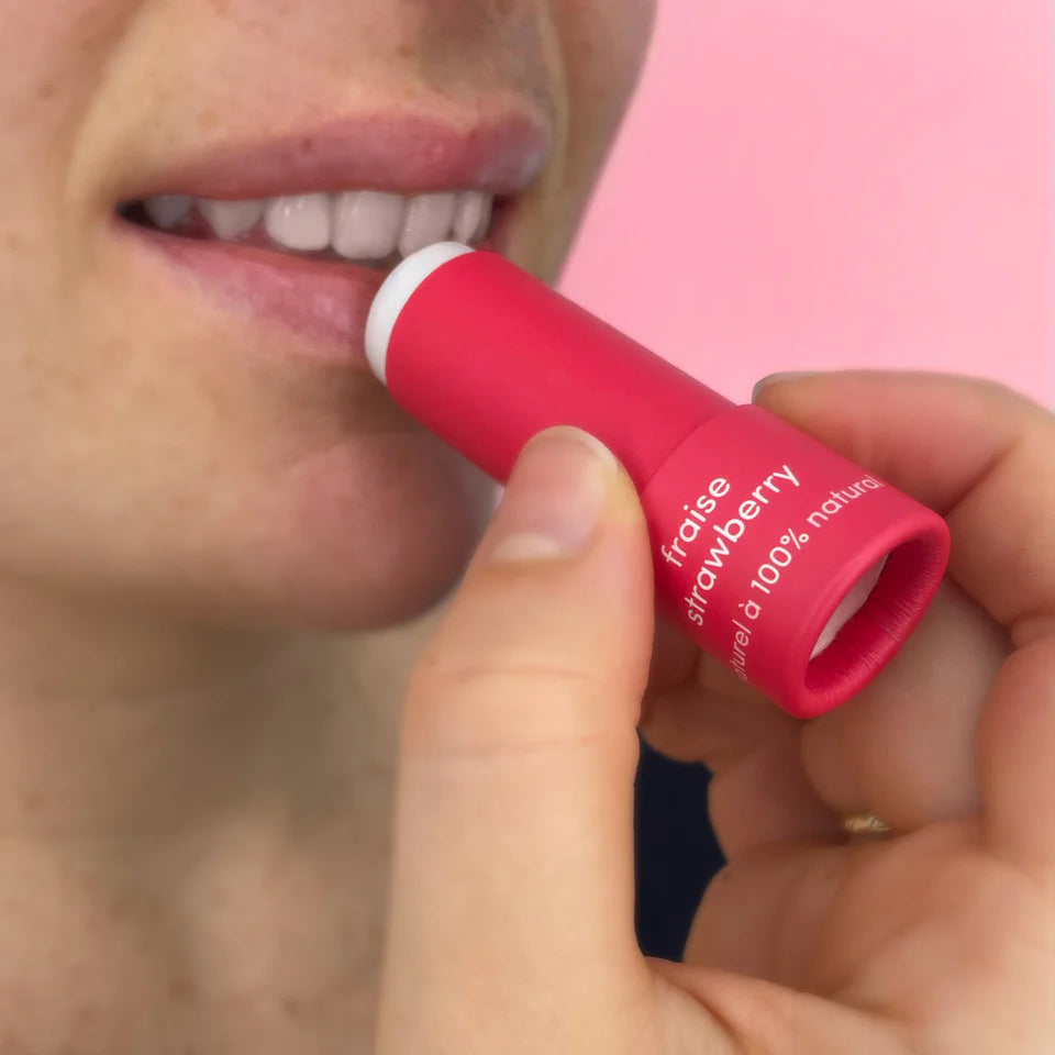 Person applying strawberry-flavored lip balm with a pink background