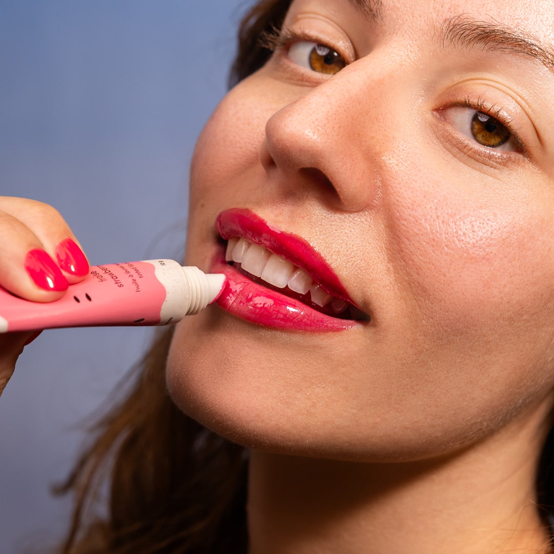 Woman applying pink lip gloss to her lips with a blue background
