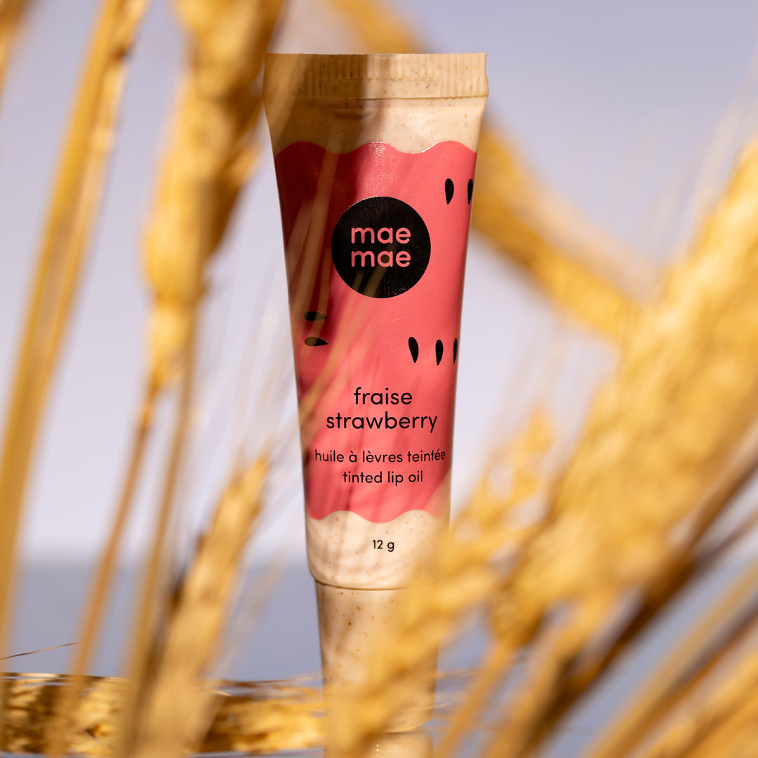 Lip balm tube labeled 'mae mae' with strawberry flavor in front of wheat stalks
