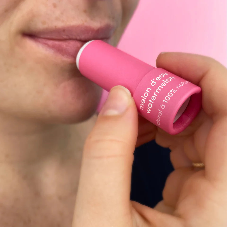 Person applying pink lip balm labeled 'melon d'eau watermelon' to their lips.