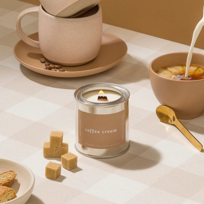 Candle labeled 'coffee cream' with a cup, bowl, and cookies on a table.