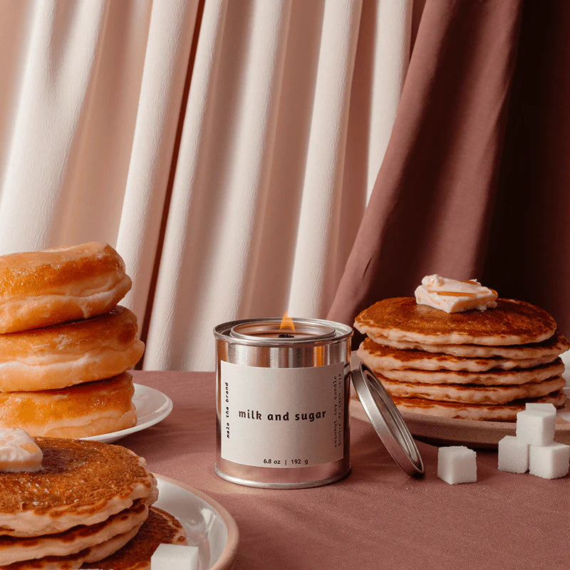 Stacks of pancakes and donuts with a can labeled 'milk and sugar' on a table.