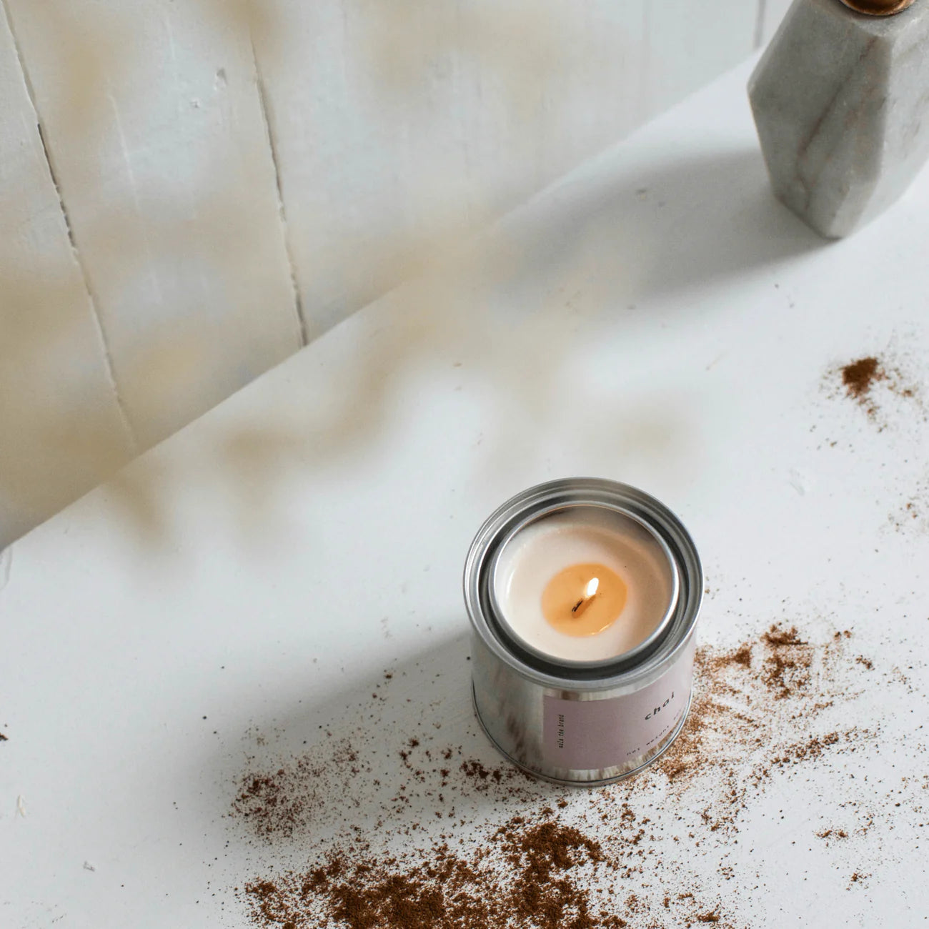 Candle in a metal can on a white surface with cinnamon spice around it