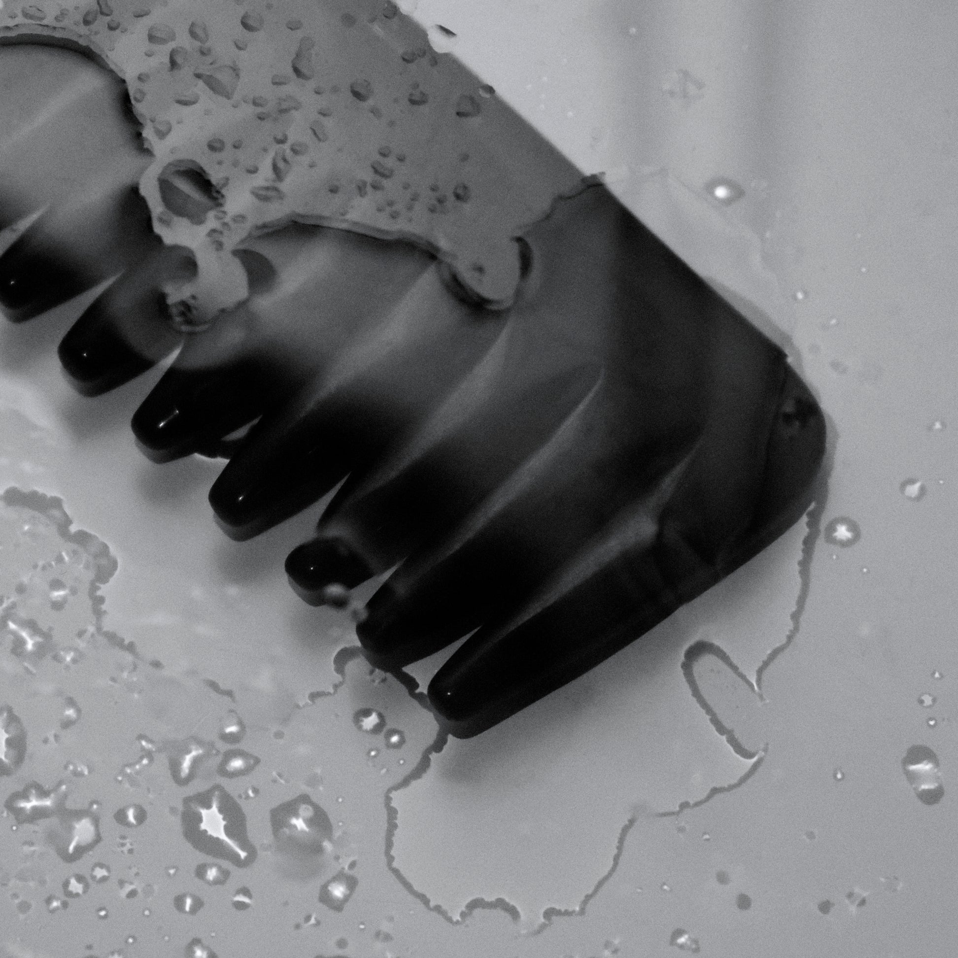 Black rubber glove with lace on a gray surface with water droplets