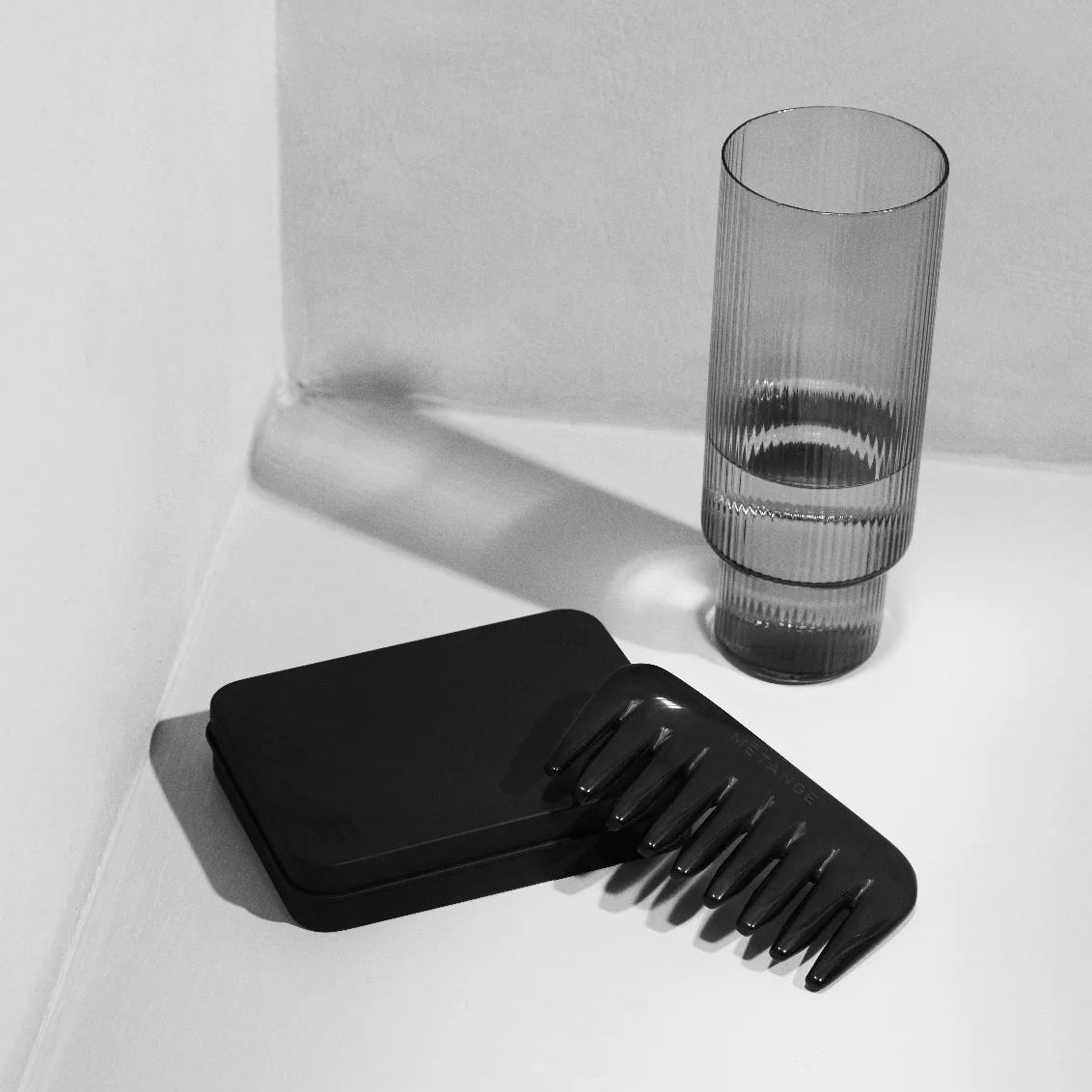 Black comb and hairbrush set on a white surface with a glass in the background