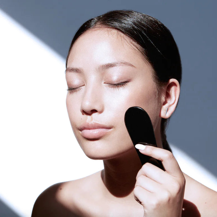 Woman applying makeup with a brush on a neutral background