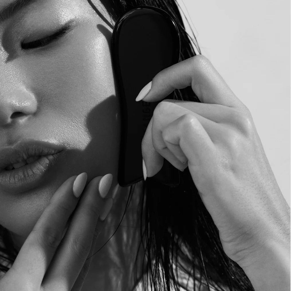 Black and white close-up of a person using a hairbrush on their hair.