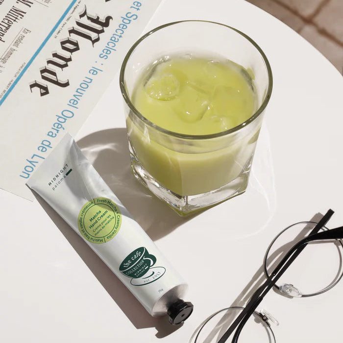 Glass of green liquid with ice cubes, tube of hand cream, and eyeglasses on a newspaper.
