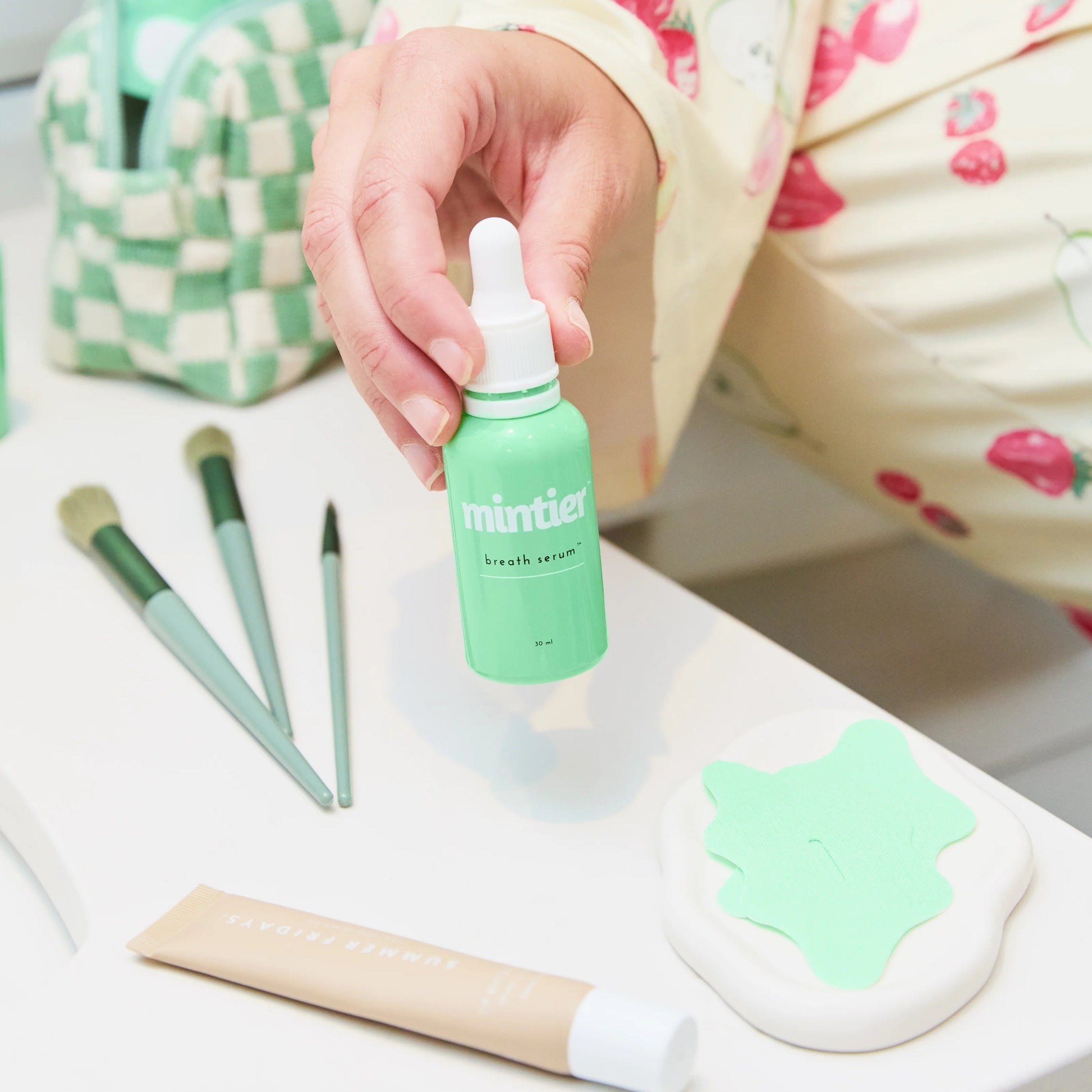 Person holding a green bottle labeled 'miniso' with makeup brushes and a pouch on a table.