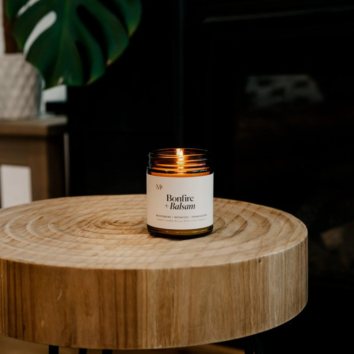 Candle labeled 'Bonfire & Balsam' on a wooden table with a dark background