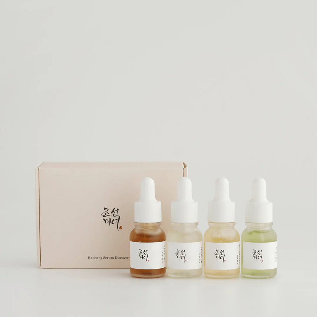 Set of four skincare serum bottles with a beige box on a light gray background
