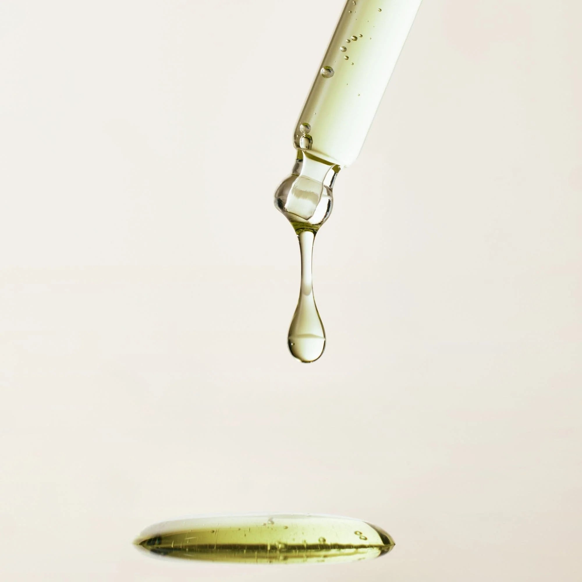 Close-up of a dropper with a drop of liquid on a light pink background