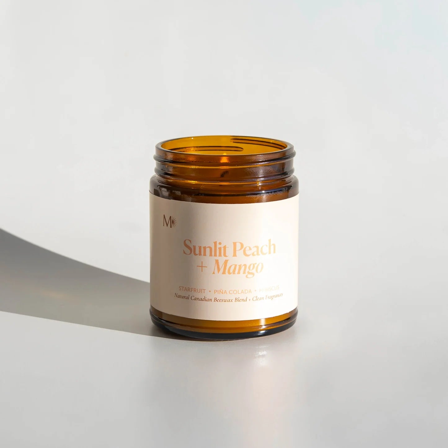 Candle jar with 'Sunlit Peach + Mango' label on a light background