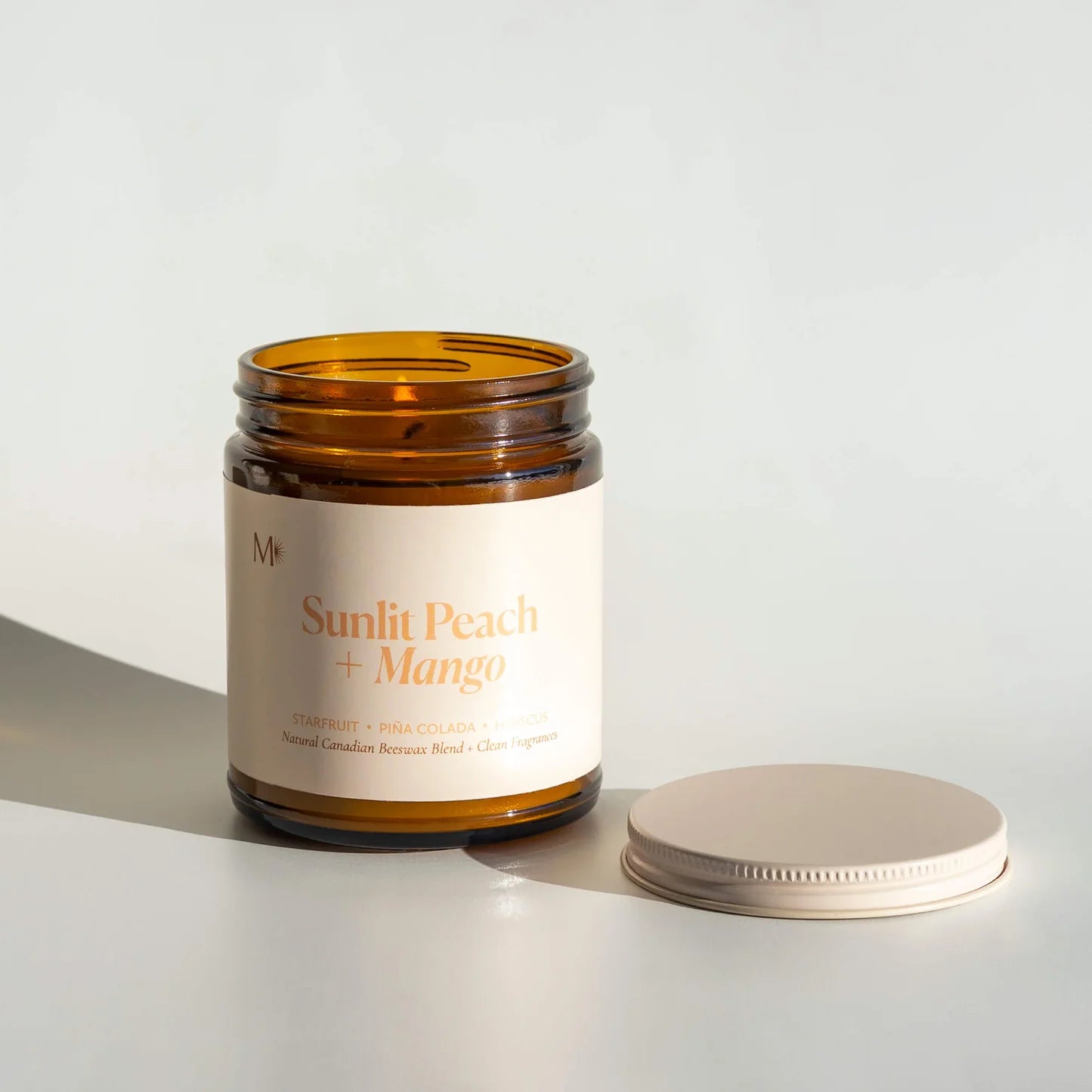 Candle with 'Sunlit Peach + Mango' label on a white background