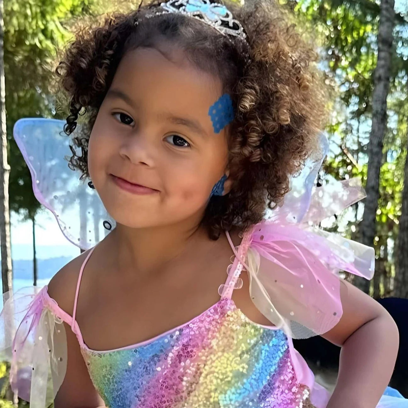 Young girl in a fairy costume standing outdoors with trees in the background