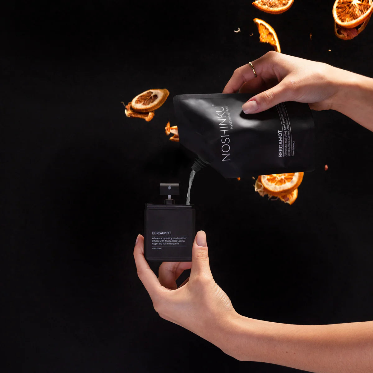 Person holding a black Noshkin perfume bottle and packaging against a dark background with orange slices.
