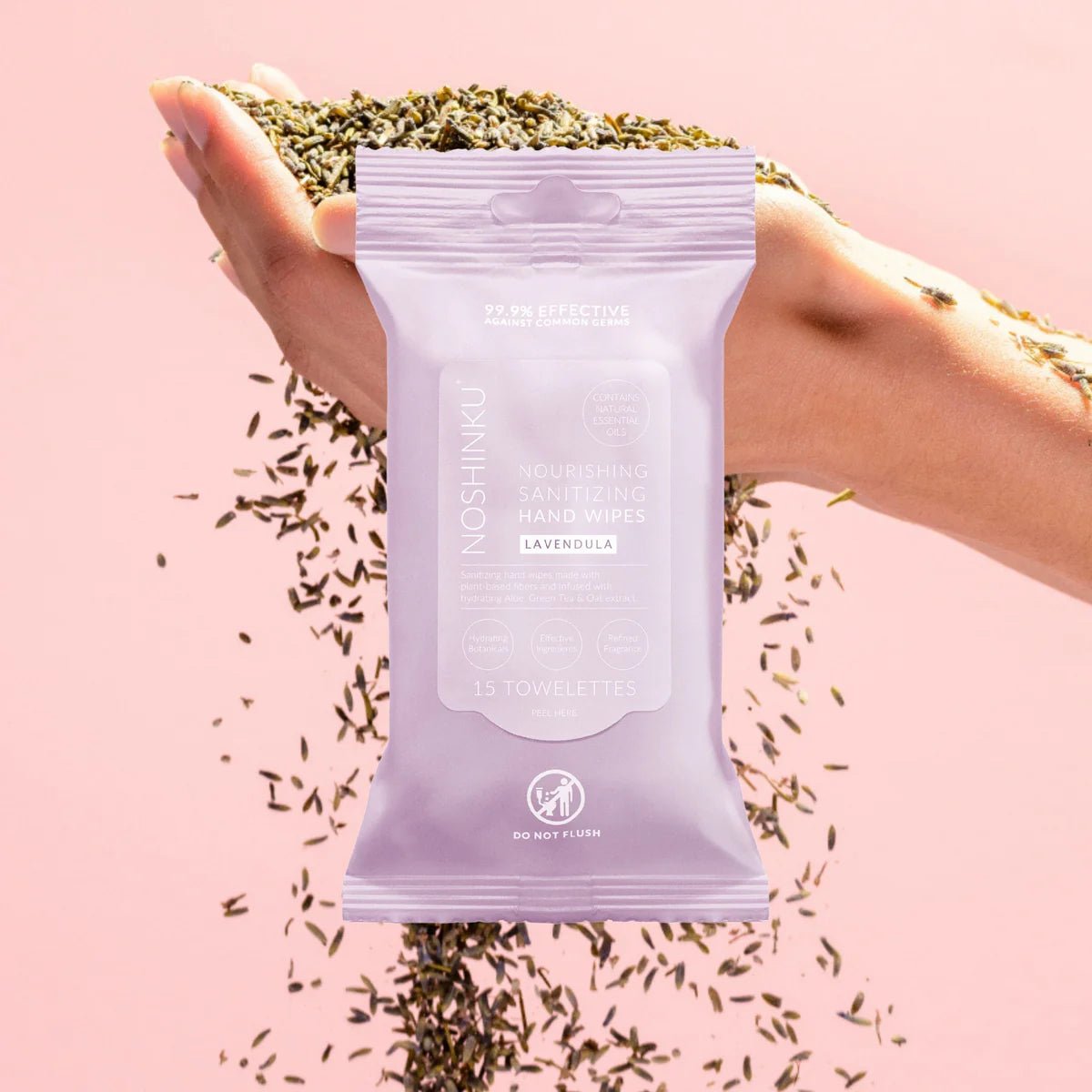 Hand holding a package of lavender hand wipes against a pink background with scattered lavender leaves.