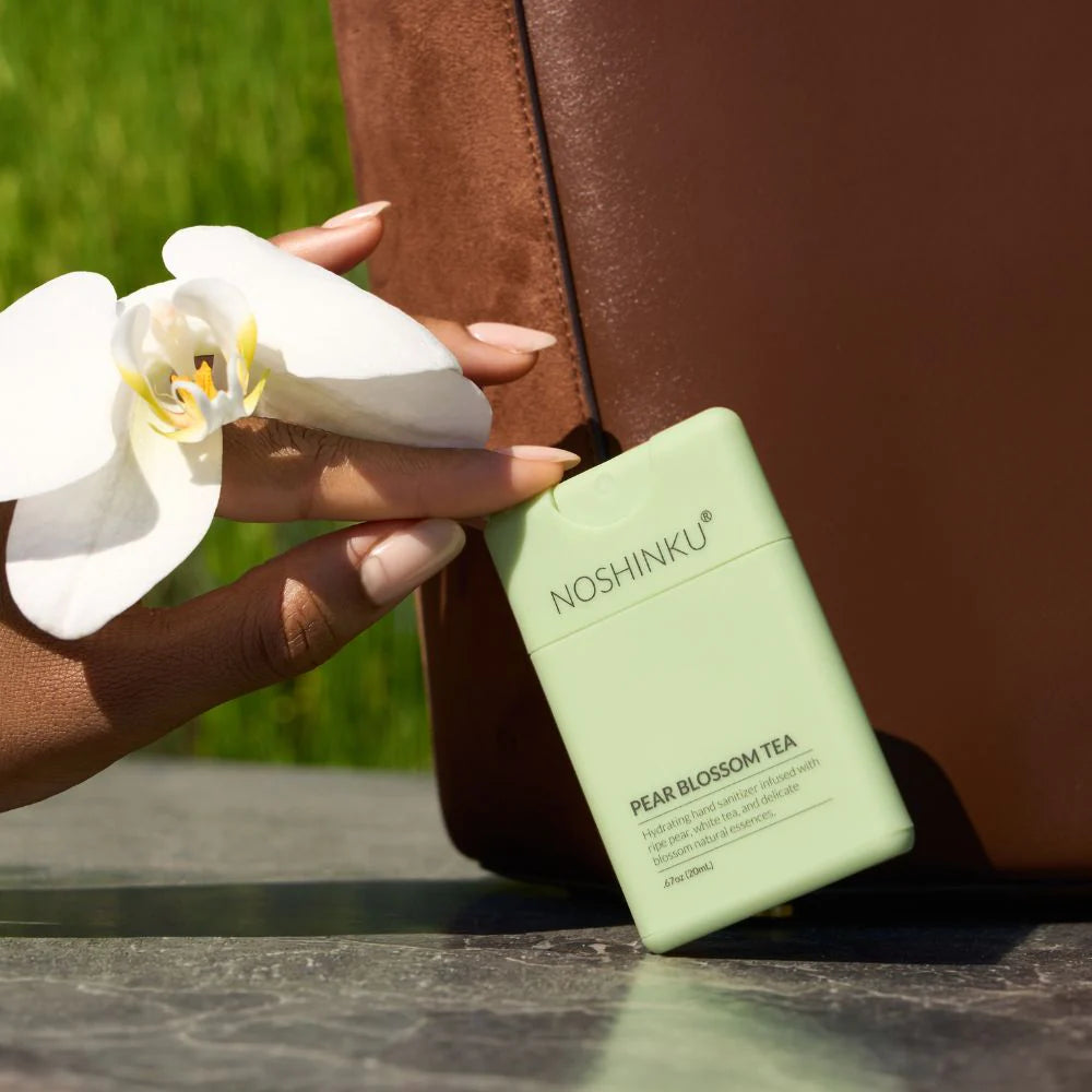 The Pharmacy Lab Noshinku Pear Blossom White Tea Pocket Sprayer beside orchid flower and handbag for travel-friendly hand care