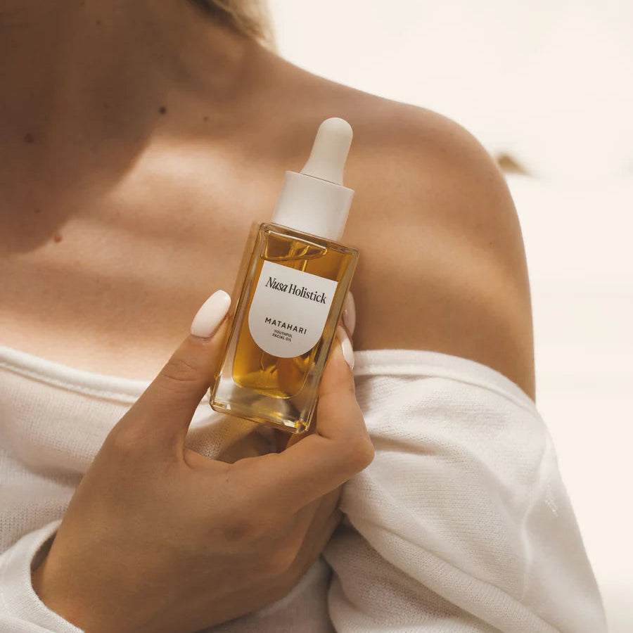 Hand holding a bottle of Aesop skincare product against a neutral background