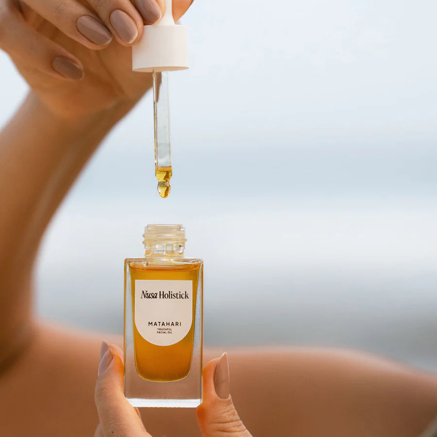 Hand holding a dropper over a bottle labeled 'Nuxe' with a blurred background