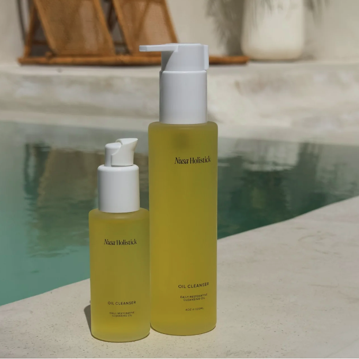 Two bottles of Nuxe Holistic Oil Cleanser on a surface with a blurred background