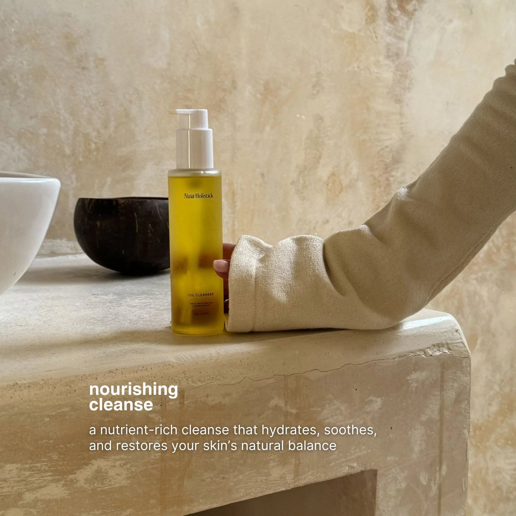 A bottle of nourishing cleanse by Northlight sits on a stone counter, with a person's arm resting beside it against a textured beige wall.