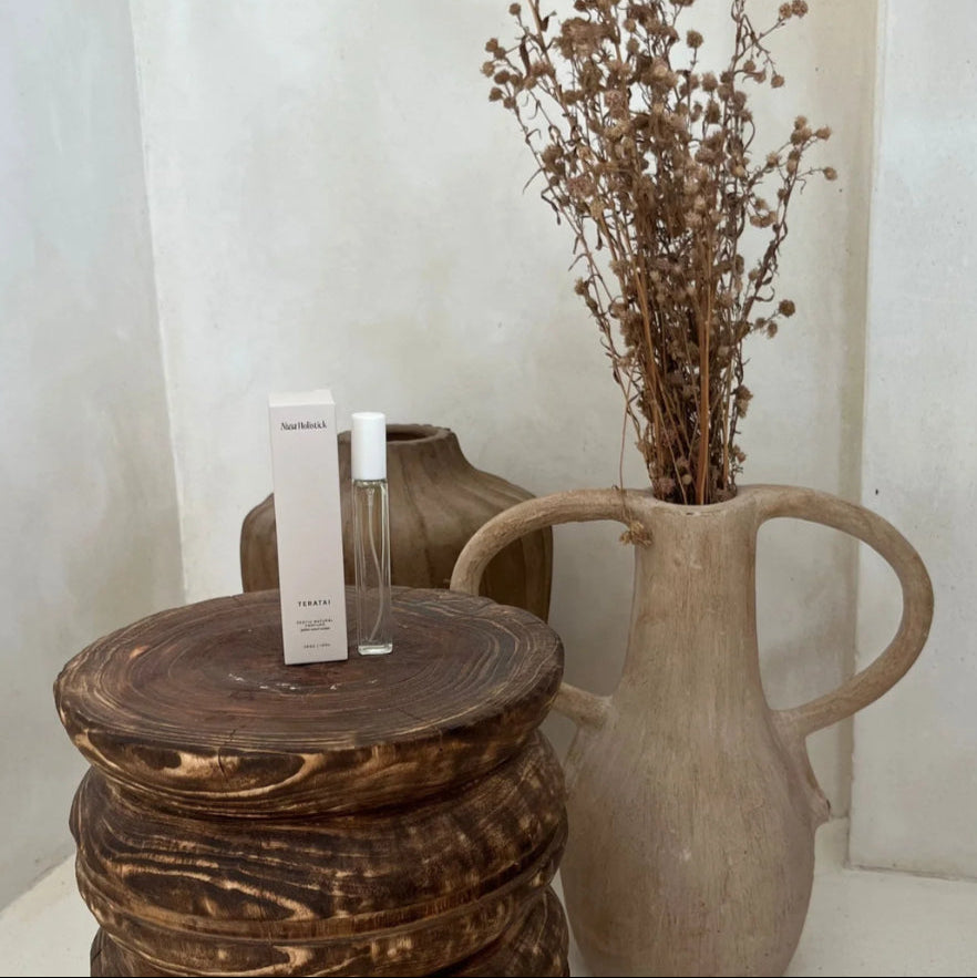 Wooden stool with a bottle and box, next to a large vase with dried flowers on a neutral background