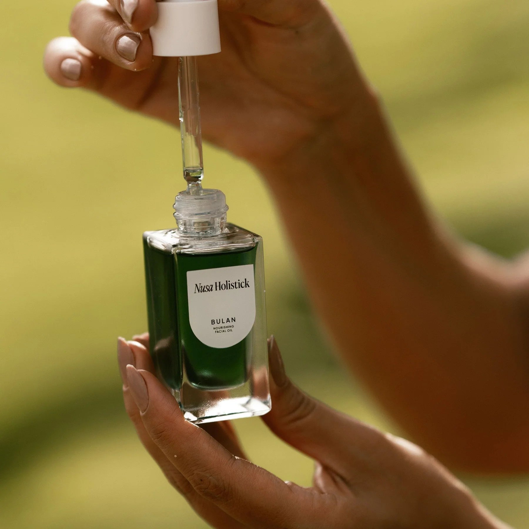 Hand holding a green dropper bottle with a blurred natural background