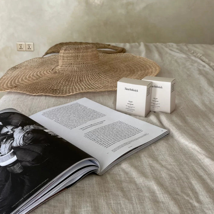 Open book, box, and straw hat on a textured surface with a neutral wall background