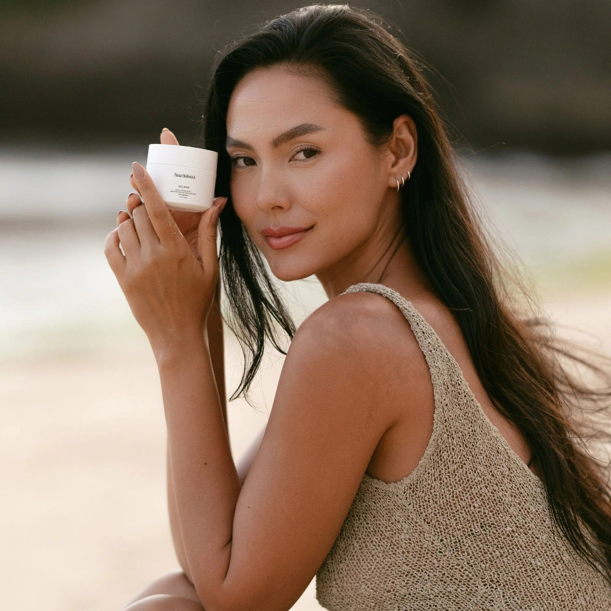 Woman holding a skincare product on a beach