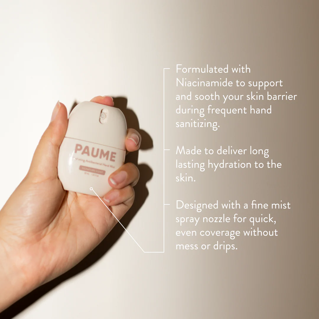 Hand holding a PAUME hand sanitizer bottle with product details on a beige background