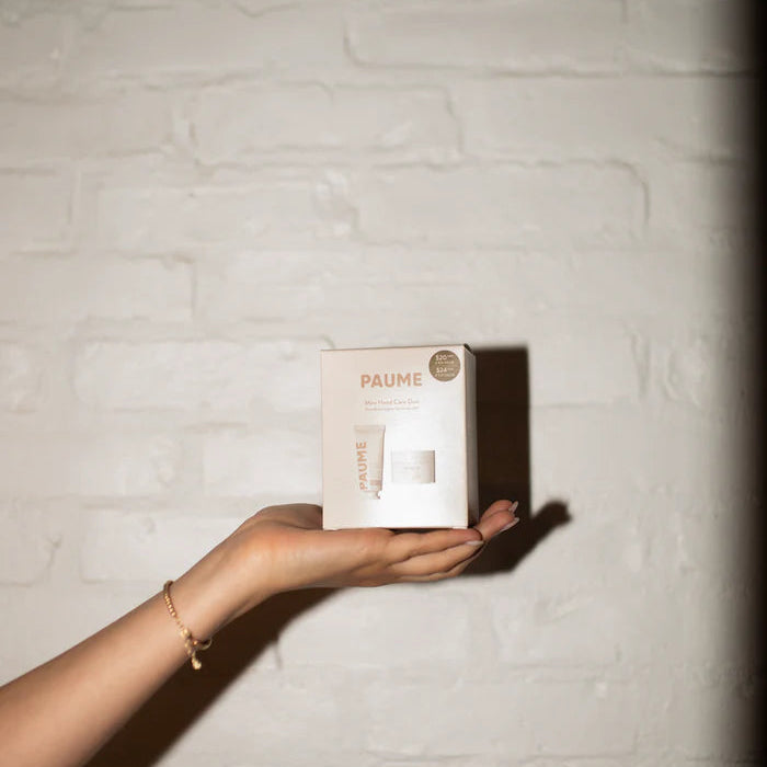 Hand holding a Paume box against a textured white wall