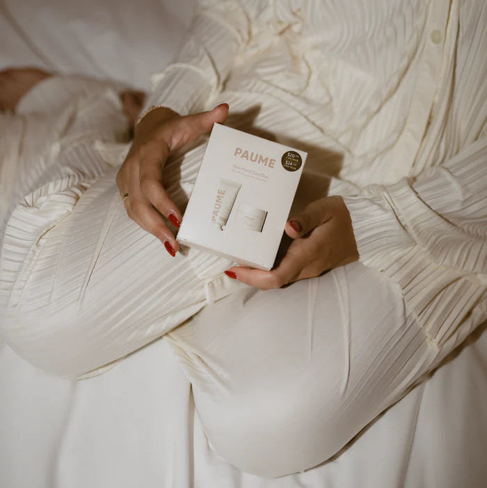 Person holding a skincare product box labeled 'PAULINE' in a white robe.
