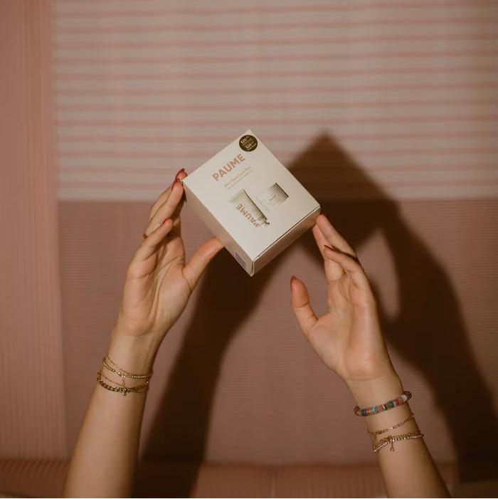 Person holding a skincare product box labeled 'PAURIE' against a striped wall.