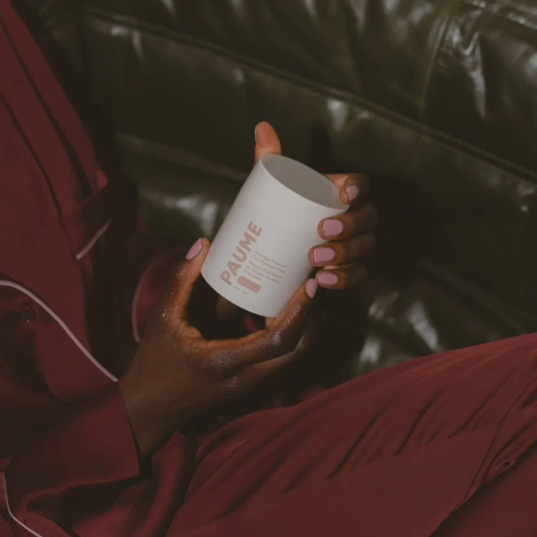 Person holding a white cup with 'PAUME' branding on a dark leather couch.