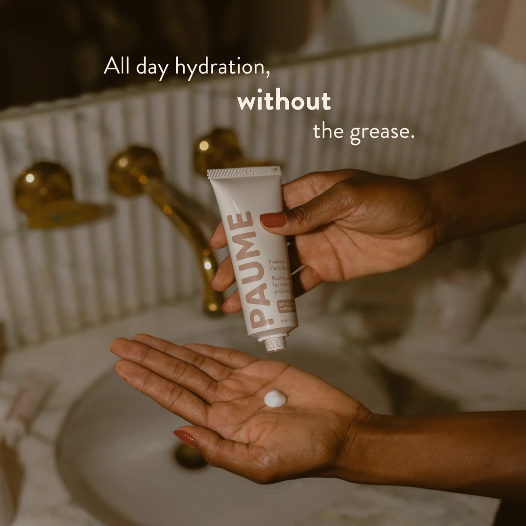 Hand holding a tube of PAUME product with text about hydration in a bathroom setting