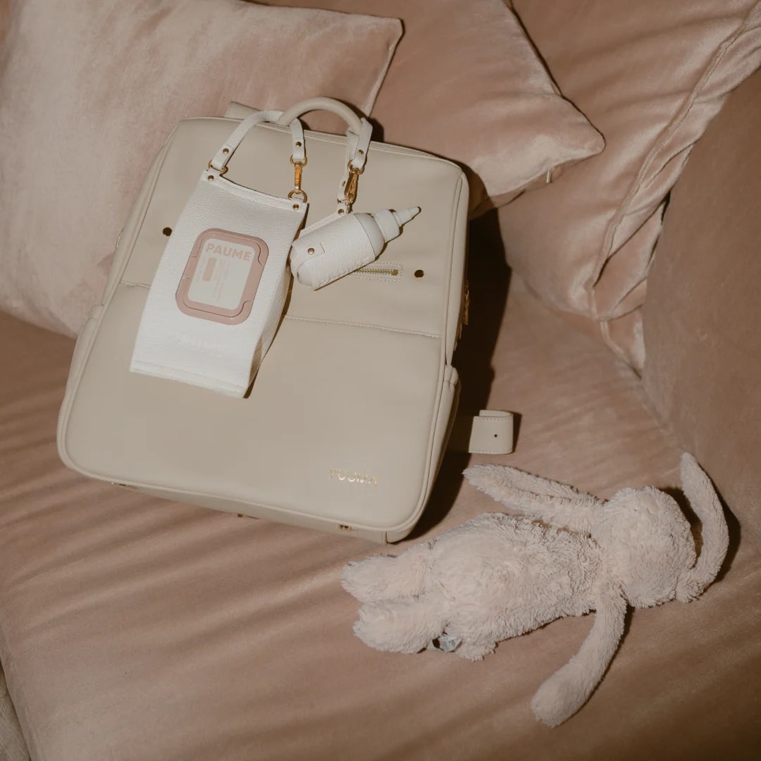 Beige handbag with a baby bottle and toy on a beige surface